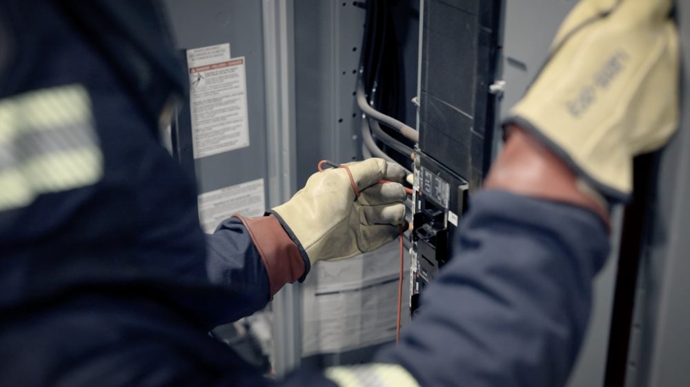 person in protective gear performing maintenance on an electrical panel